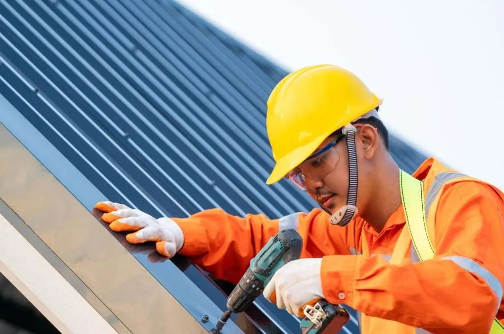 Worker in safety gear drilling on a metal roof