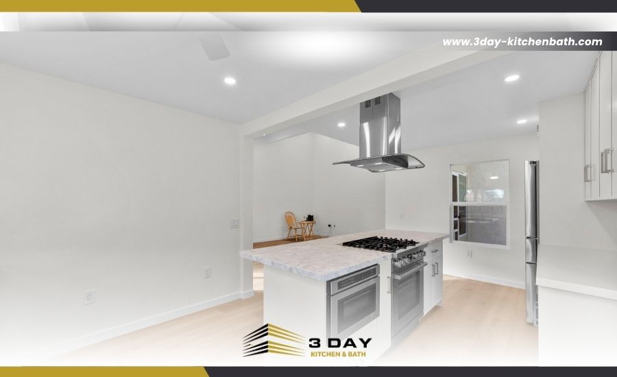 A modern white kitchen featuring an island with a marble-patterned countertop, a built-in gas stove, stainless steel appliances, and light wood flooring.