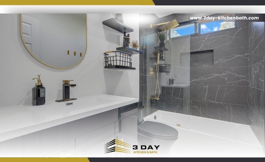 Modern bathroom remodel with a white vanity, a round gold mirror, and a shower-tub combo lined with black marble-look tile, branded by 3 Day Kitchen & Bath.