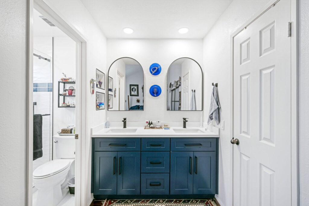 Double vanity with navy blue cabinets two arched mirrors and blue decorative plates on a white wall