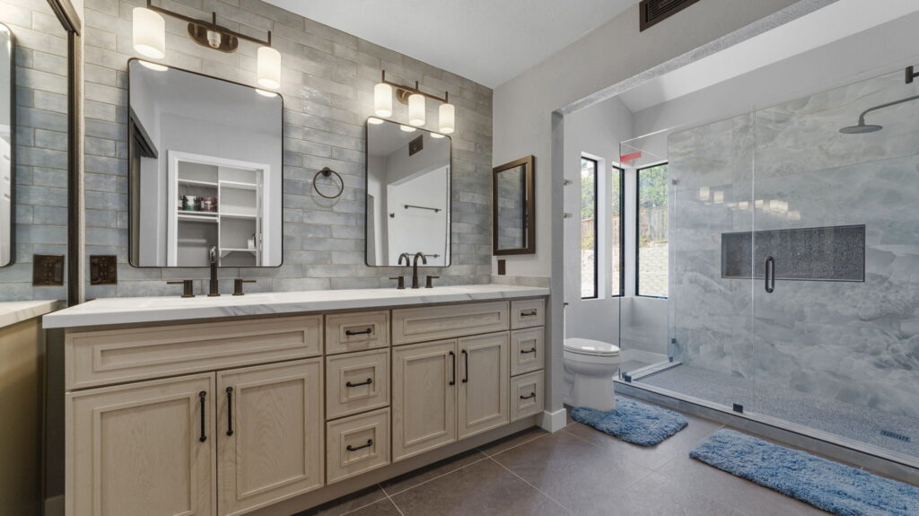 Double vanity with white countertop light wood cabinets and two rectangular mirrors under modern wall sconces in a bright bathroom