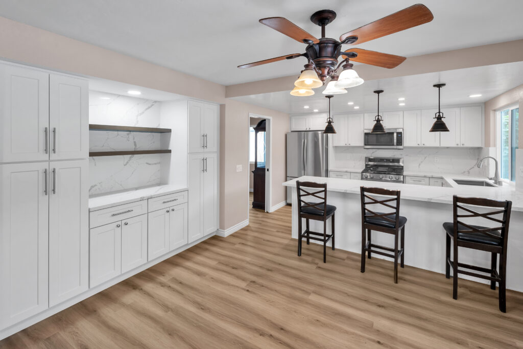 Bright white kitchen with marble backsplash, island seating, and stainless appliances under a ceiling fan light.